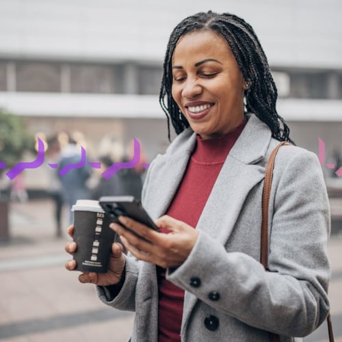 Photo of a smiling woman outside of an office building, which is blurred in the background. She is looking at her phone in one hand and carrying a coffee cup in the other.  Across the frame in the background run a series of small purple icons representing text traffic.